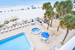 A pool area with lounge chairs and umbrellas, a hot tub, and a view of the beach.