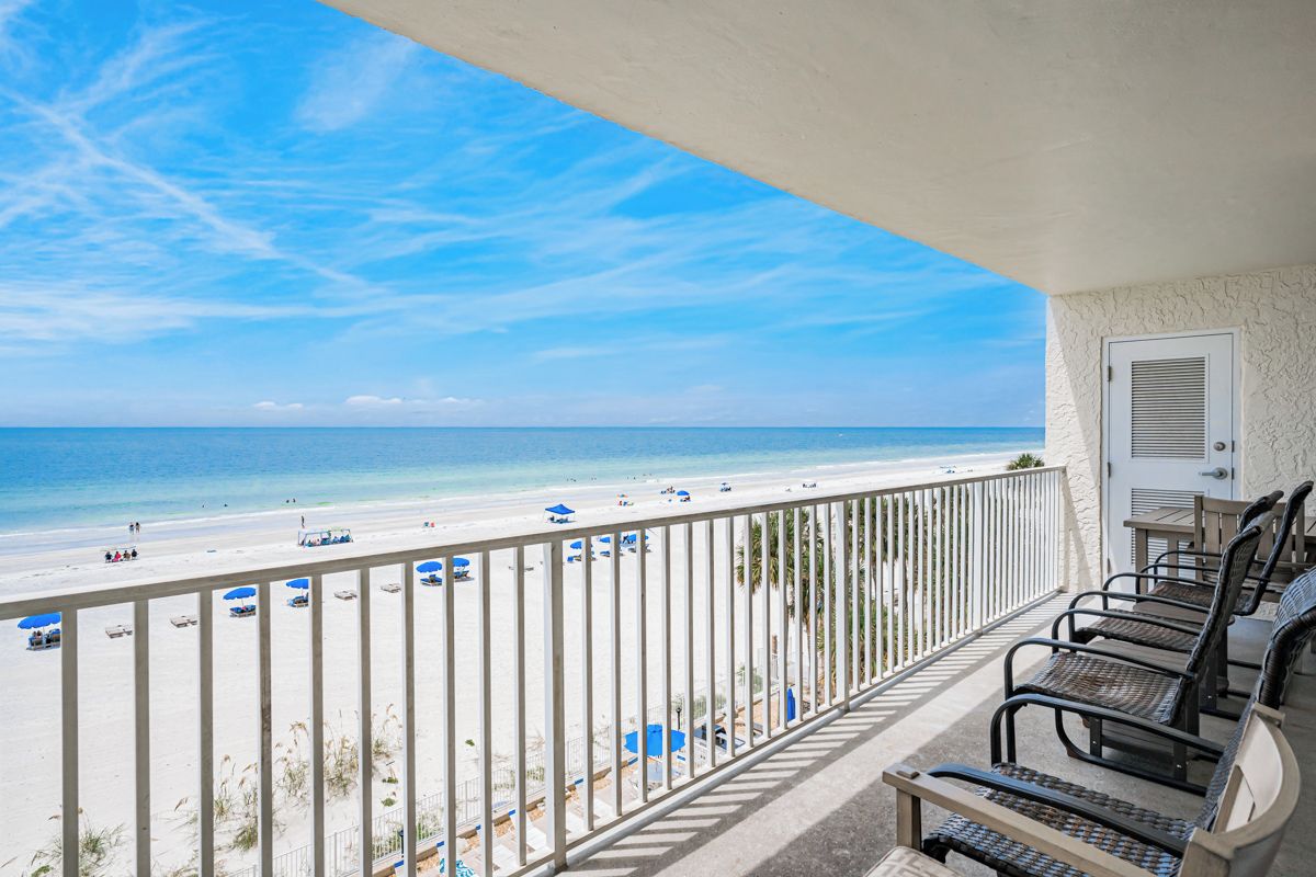 Een balkon met uitzicht op het strand, een deur en een zithoek met stoelen.