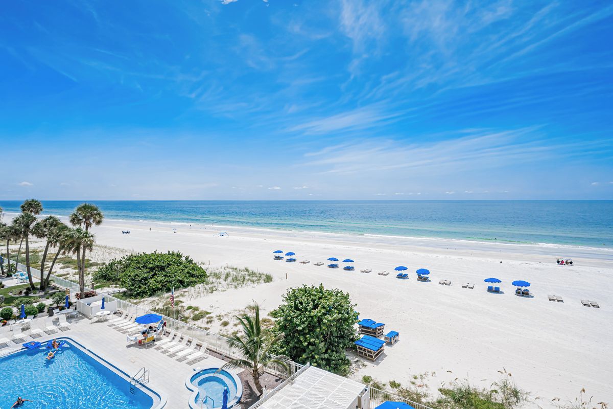 A beach resort with a swimming pool, beach umbrellas, and a clear view of the ocean.