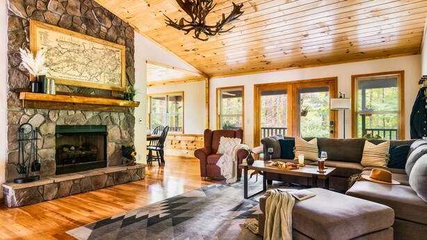 Una sala de estar acogedora con chimenea de piedra, techo de madera y ventanas amplias.
