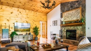 Una sala de estar acogedora con chimenea de piedra, techo de madera y un televisor de pantalla plana grande.