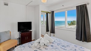 Ein Hotelzimmer mit einem Bett, einem Fernseher auf einer Holzkommode, einem Deckenventilator und einem Fenster mit Blick auf den Strand.