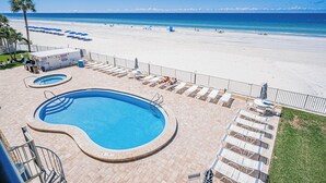 A pool area with two pools, lounge chairs, and a beach view.