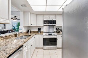 A kitchen with white cabinets, a granite countertop, a stainless steel refrigerator, a microwave, an oven, and a sink.