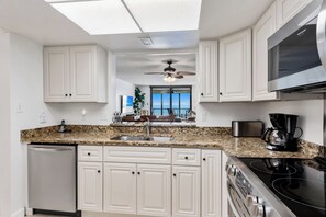 A kitchen with white cabinets, a granite countertop, a stainless steel refrigerator, a black stove, and a ceiling fan.