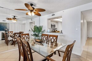 A modern dining area with a glass table, wooden chairs, and ceiling fans. - Sand Castle III 403 - GULF FRONT Condo! (Indian Shores)