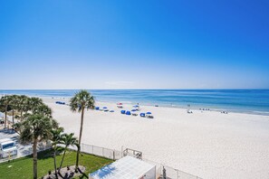 A beach with a clear sky, palm trees, and umbrellas.