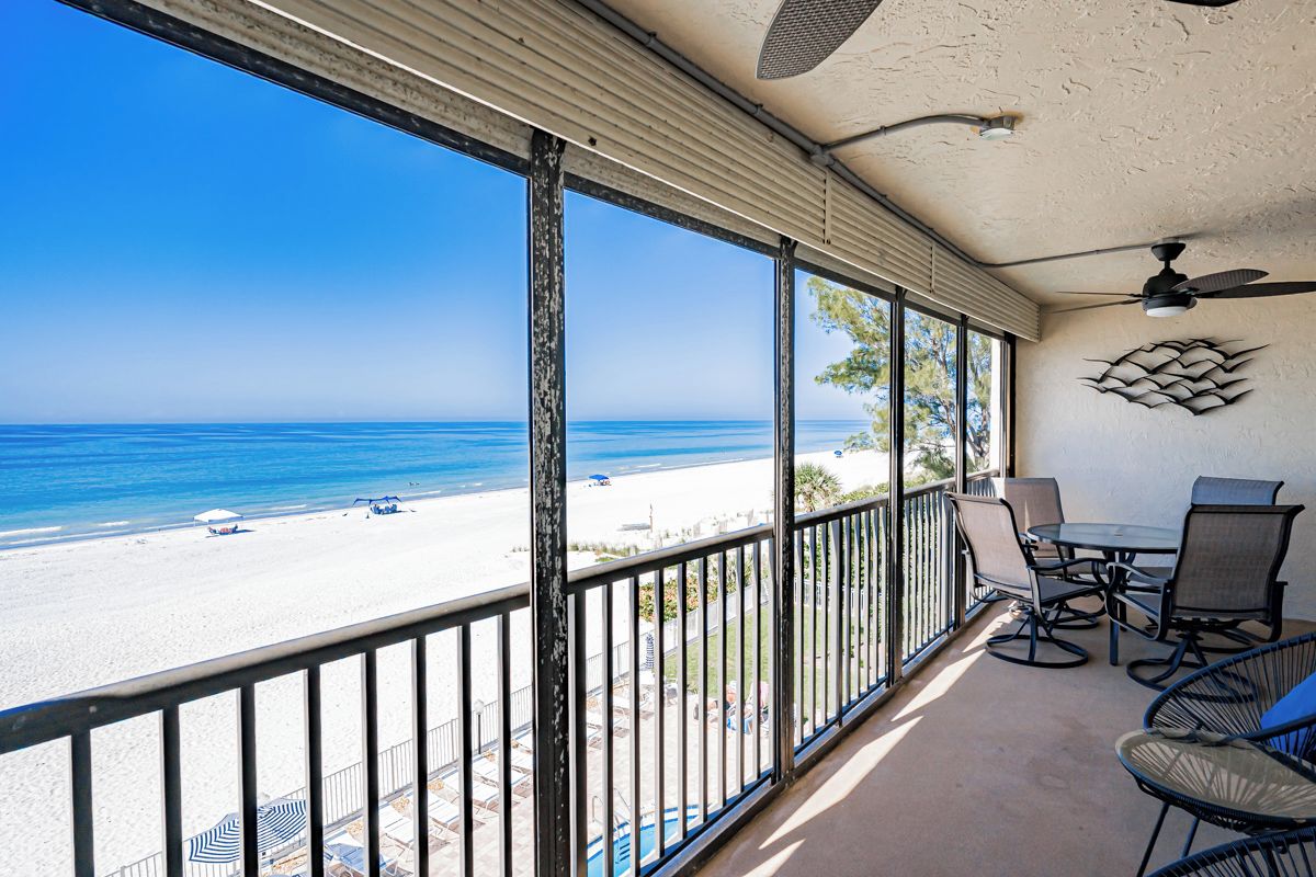 A balcony with a view of the beach, a ceiling fan, and outdoor furniture.