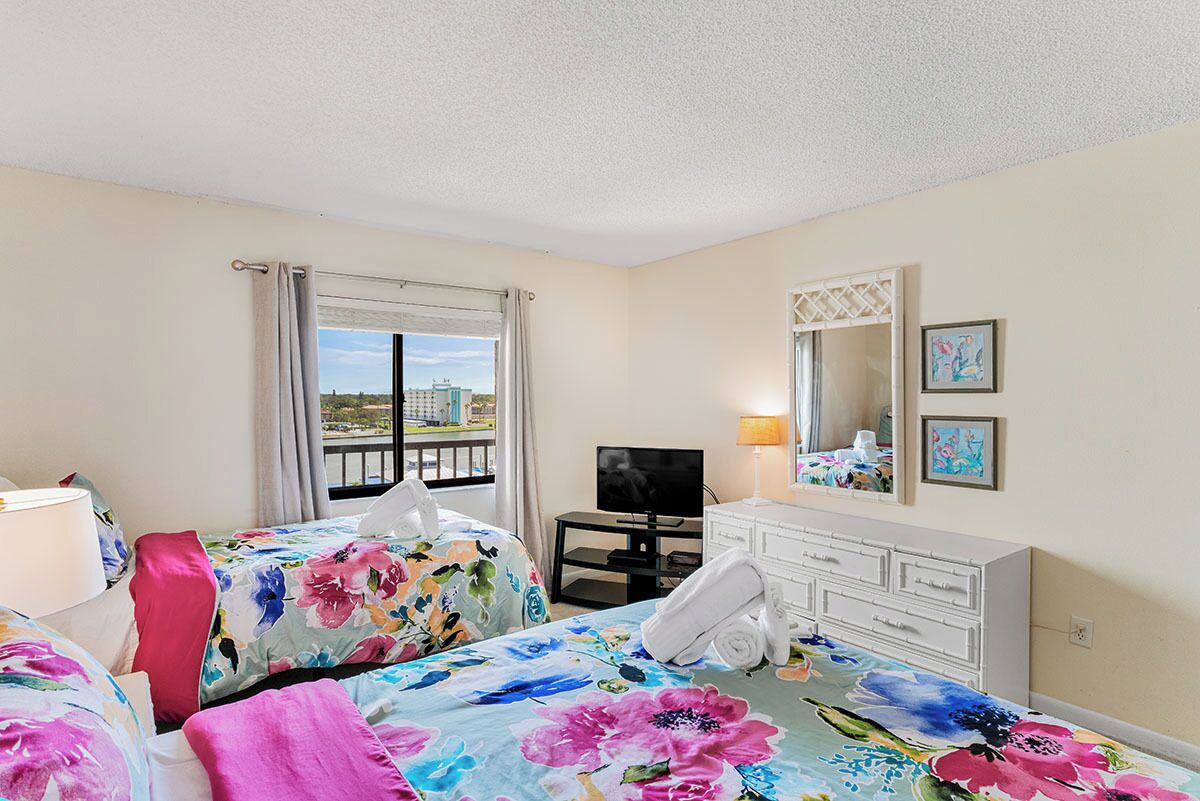 Quarto de hotel com duas camas, televisão, mesa, telefone e janela com vista.