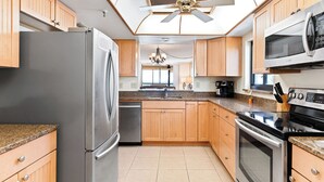 A modern kitchen with wooden cabinets, stainless steel appliances, and a ceiling fan.