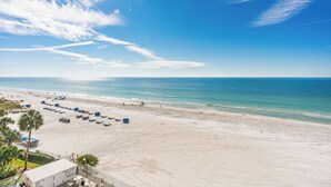 A beach with clear skies, a sandy shore, and several umbrellas and lounge chairs.