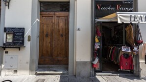 A storefront with a wooden door, a sign for 'Veccia Firenze,' and a clothing rack with prices. - Santa Croce View 1 by Mmega (Firenze)