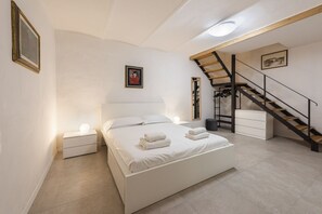 Une chambre à coucher avec un lit, des tables de chevet, un escalier et un tableau encadré au mur.