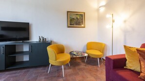 A living room with a flat-screen TV, two yellow chairs, a red sofa, a small table, and a painting on the wall. - Santa Croce View 2 apartment by Mmega (Firenze)