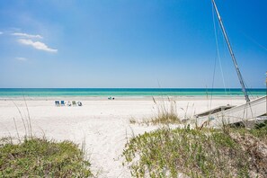 A beach with white sand, a clear blue sky, and a few beach chairs.
