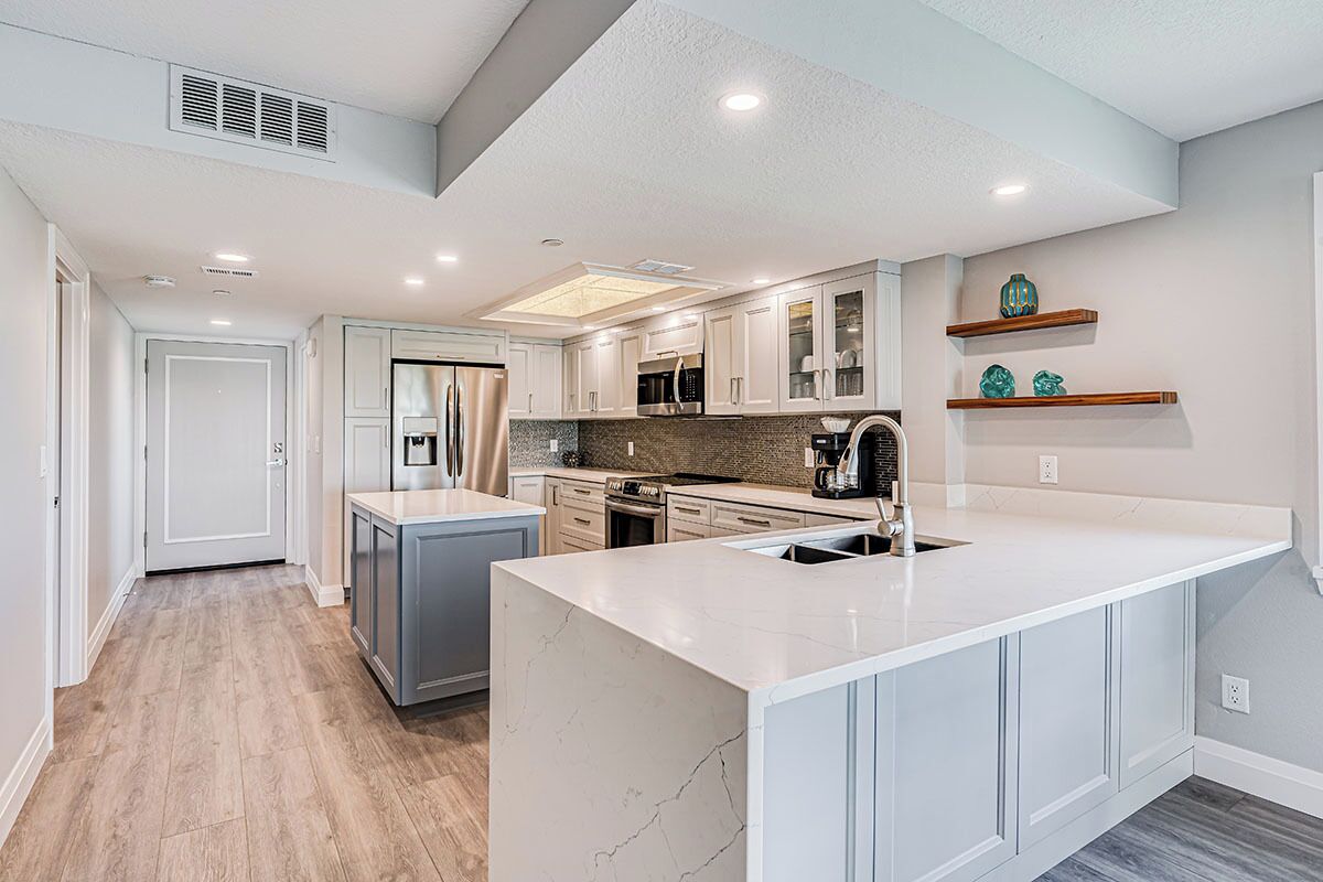 A modern kitchen with white cabinetry, a marble island, and a built-in oven.