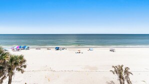 A beach with white sand, clear blue sky, and calm sea. There are umbrellas and beach chairs.