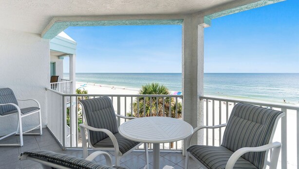 A balcony with white wicker furniture, a round table, and a view of the beach.