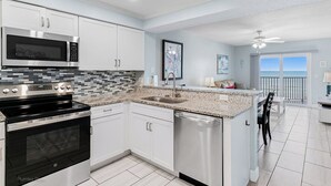 A modern kitchen with white cabinets, a stainless steel microwave, a black stove, and a granite countertop.