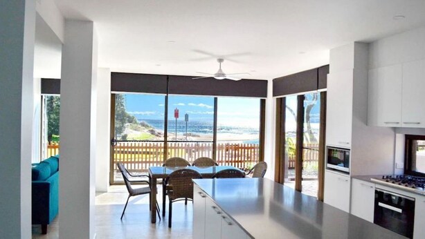 Una cucina moderna con una grande isola, una zona pranzo con vista sulla spiaggia e una ventola a soffitto.