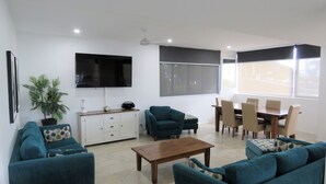 Un soggiorno con divani color petrolio, un tavolino in legno, una televisione e una zona pranzo con sedie e tavolo.