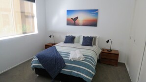 Una camera da letto con un letto, due comodini, una finestra e un quadro appeso al muro raffigurante una pinna di balena.