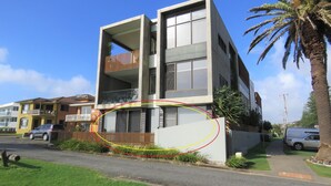 Un edificio moderno a due piani con balconi, un ingresso con cancello e una palma sullo sfondo.