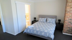 A bedroom with a bed, two bedside tables, a nightstand, a door, and a brick wall.