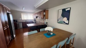 A modern kitchen with wooden cabinets, a central island, and a dining area with a table and chairs. - Comfortable Townhouse with WIFI right in the heart of town. (South West Rocks)