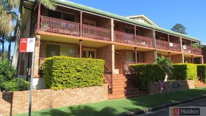 A two-story brick building with a balcony, a 'No Stopping' sign, and well-maintained hedges. - Comfortable Townhouse with WIFI right in the heart of town. (South West Rocks)