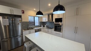 A modern kitchen with stainless steel appliances, a large island, and pendant lighting. - CAMEO COURT UNIT 9 - Beautiful Unit close to town centre. (South West Rocks)