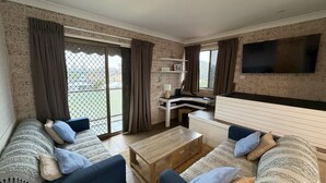 A living room with a sofa set, a coffee table, a TV mounted on the wall, and a sliding glass door leading to an outdoor area. - CAMEO COURT UNIT 9 - Beautiful Unit close to town centre. (South West Rocks)