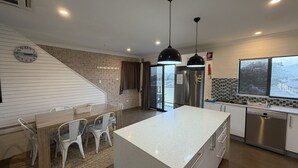 A modern kitchen with a central island, stainless steel appliances, and a view of a snowy landscape through the window. - CAMEO COURT UNIT 9 - Beautiful Unit close to town centre. (South West Rocks)