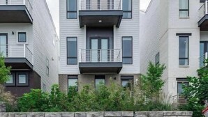 En modern bostadsbyggnad med flera våningar, balkonger, en mur av natursten och en stenlagd trottoar.