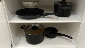 Une étagère de cuisine avec une passoire, une poêle, une casserole avec un couvercle et une petite casserole.