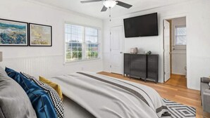 Une chambre moderne avec un lit, un ventilateur de plafond, une télévision et une fenêtre équipée de stores.