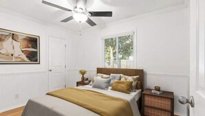 Une chambre à coucher avec un lit, un ventilateur de plafond, une fenêtre et une table de chevet.
