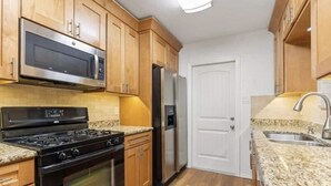 Une cuisine avec des meubles en bois, un four à micro-ondes en acier inoxydable, une cuisinière noire, un réfrigérateur en acier inoxydable et un comptoir en granit.