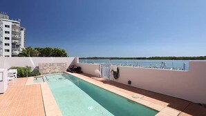 A rooftop pool with a clear view of the sea, a stone wall, and a white building in the background. - Sitka Penthouse Apartment (Maroochydore)