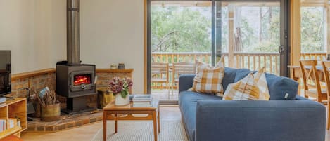 A cozy living room with a fireplace, a sofa, and a balcony with wooden railings.