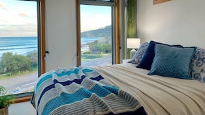 A bedroom with a large bed, two windows, and a view of the ocean. - Surf Shack - Beach Front (Separation Creek)