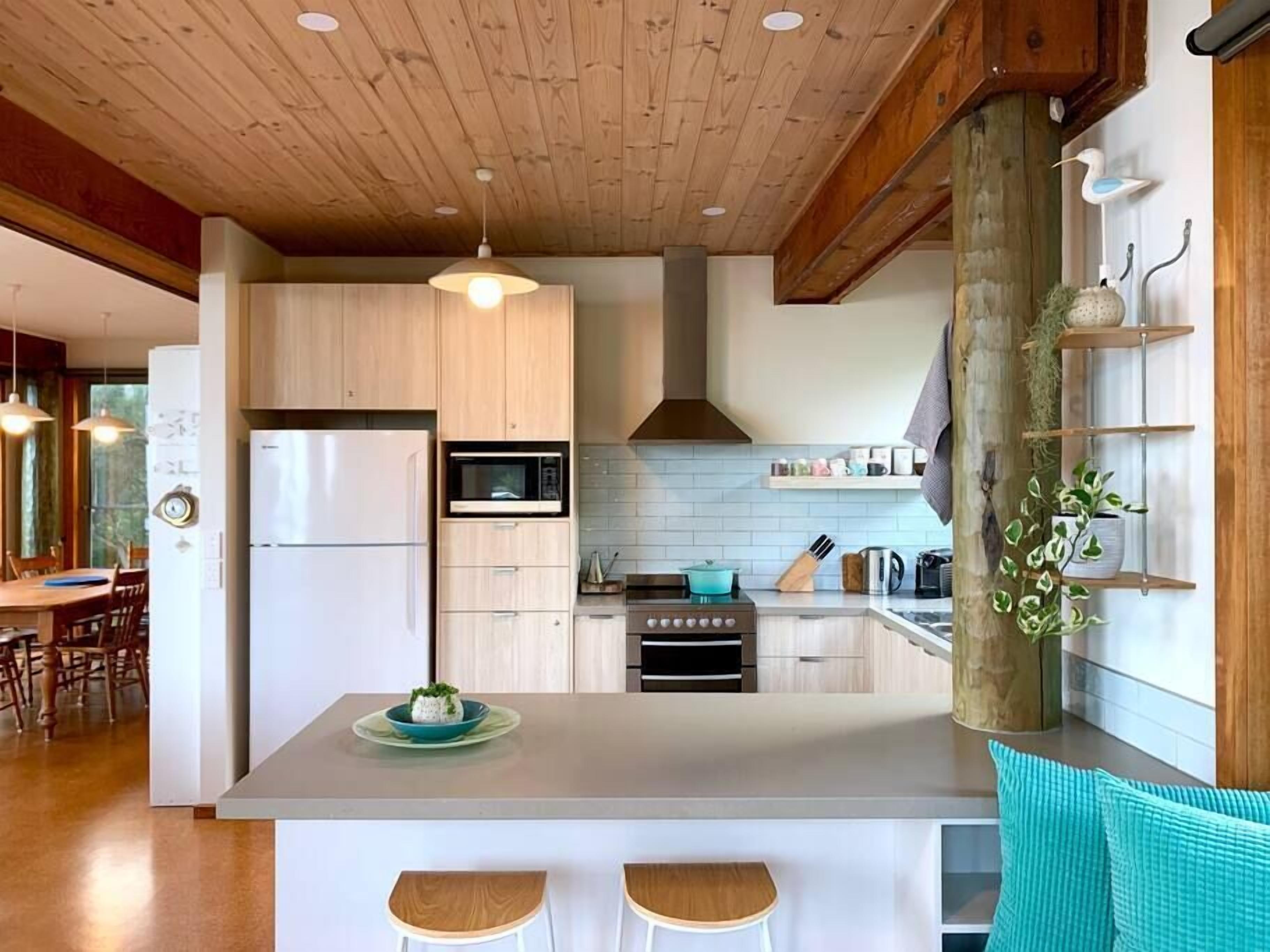 A modern kitchen with wooden cabinets, a central island with stools, a built-in oven, and a microwave.