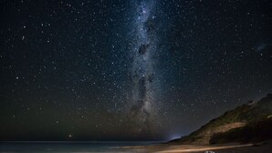 Une plage de nuit, sous un ciel étoilé où l’on peut distinguer la Voie lactée.