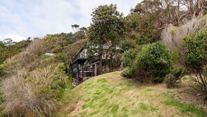 Une maison située sur une colline, dotée d’une terrasse en bois et d’un escalier menant à un balcon.