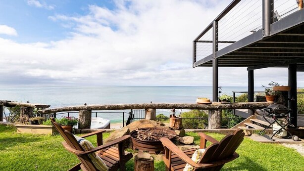 Une terrasse en bois avec un foyer, du mobilier d’extérieur et une vue sur la mer.
