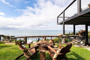 A wooden deck with a fire pit, outdoor furniture, and a view of the sea. - Y Vue - Beach Side, Spa and fire pit with Ocean Views (Wye River)