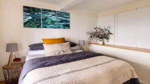 Une chambre à coucher comprenant un lit, une table de chevet, une lampe, une étagère murale avec une plante et un grand tableau abstrait au-dessus du lit.