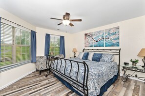 A bedroom with a bed, a chair, a ceiling fan, and a window with curtains.