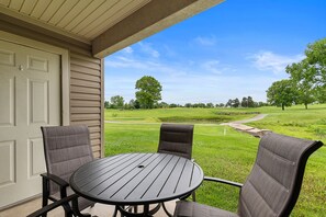A patio with a round table and two chairs, overlooking a golf course.