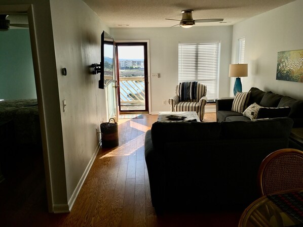A living room with a sofa, a striped armchair, and a view through a door to a balcony. - Huge condo! block from the Beach and 2 Decks with amazing views! (North Myrtle Beach)